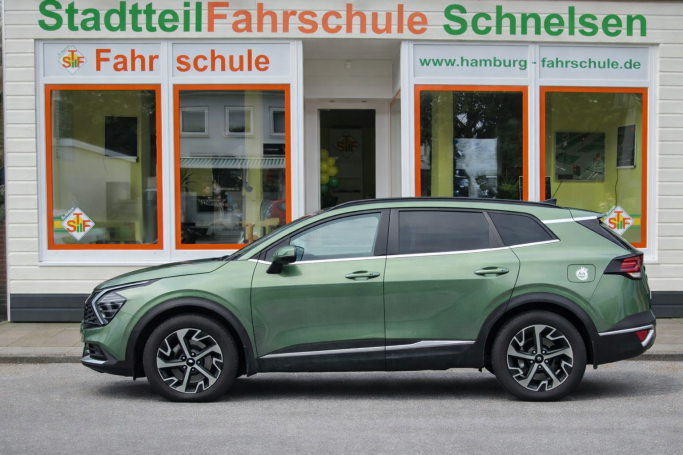 Ein grünes SUV parkt vor einer Fahrschule mit orange-weißer Beschriftung.