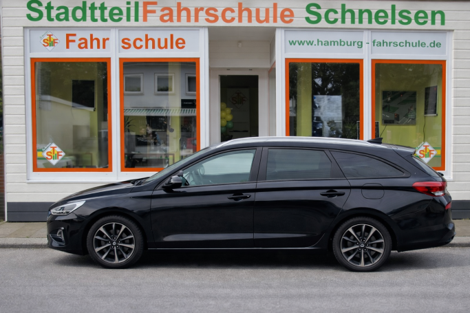 Schwarzer Kombi parkt vor der Fahrschule Schnelsen mit großer Fensterauslage.